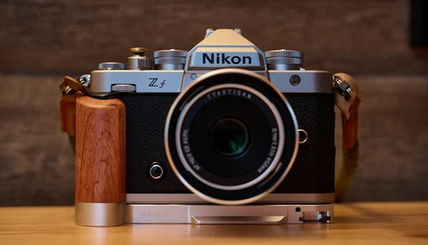 Nikon Z f mirrorless camera with wooden grip and attached lens, displayed on wooden surface.