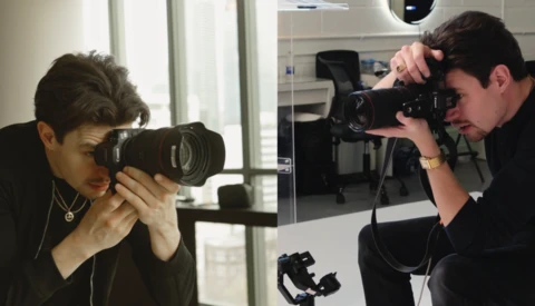 Two photographers in an office setting, each holding professional DSLR cameras with large lenses, one photographing the other.