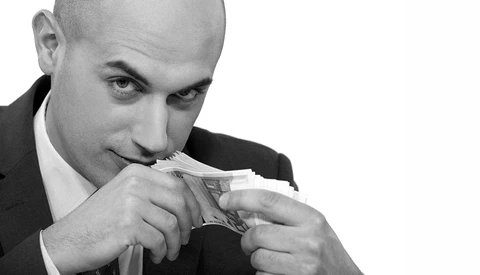 Businessman in suit holding and examining paper currency close to his face.