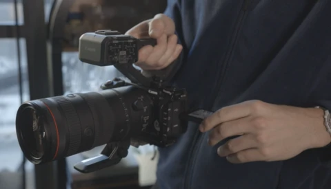Videographer operating professional cinema camera with attached monitor and telephoto lens