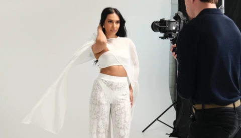 Model in white crop top and patterned pants poses during studio photoshoot with camera operator