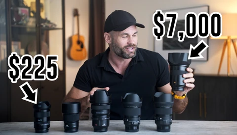 A man in a black cap and shirt displays five camera lenses arranged on a table, each labeled with prices ranging from $225 to $7,000.