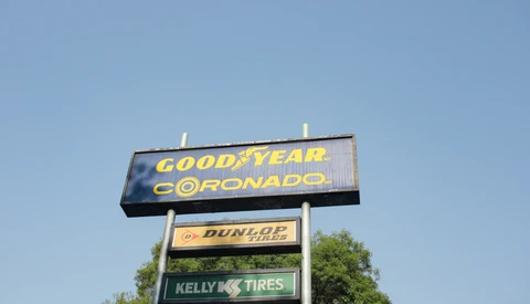 Stacked vintage tire shop signs against a clear blue sky with green tree foliage visible at the base.