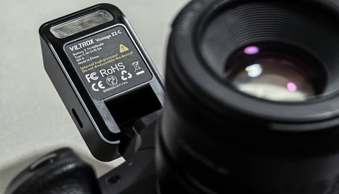 Compact camera flash unit with yellow label mounted on camera body next to telephoto lens.