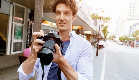 Photographer holding a DSLR camera on an urban street, demonstrating equipment handling.