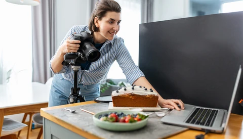 Food photographer holding a professional camera on a gimbal while shooting a styled flat-lay of produce and baked goods.