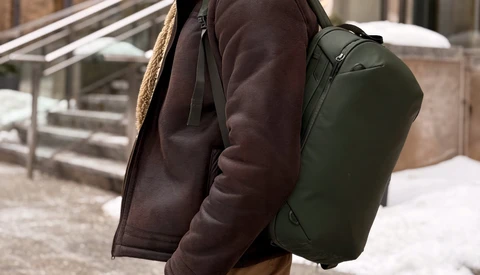 Person wearing a dark brown jacket and olive green backpack standing on outdoor steps.
