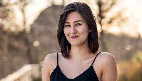 Young woman with dark shoulder-length hair smiling at camera outdoors during golden hour.