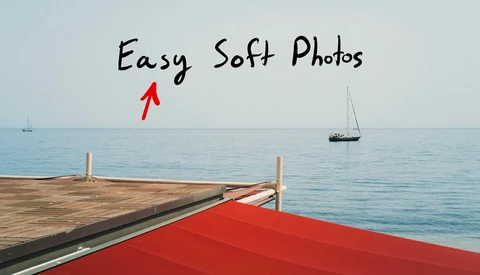 Wooden dock with red awning extending into calm blue water with sailboats in distance.