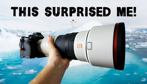 Photographer holding a white telephoto lens with red accents against an aerial landscape of blue water and snowy terrain.