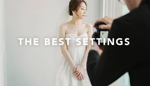 Bride in white strapless gown posing while photographer frames shot with camera.