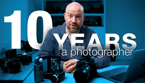 Photographer with professional camera equipment at desk with blue lighting and text overlay stating "10 YEARS a photographer."
