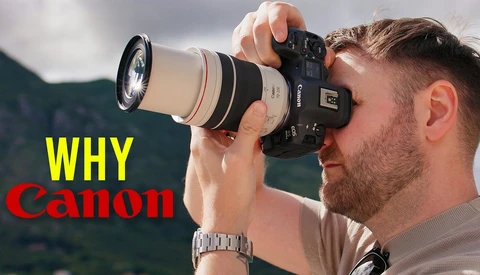 Photographer holding Canon telephoto lens to eye while composing a shot outdoors.