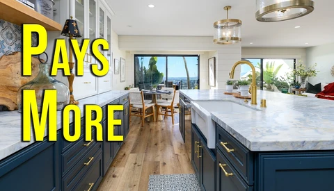 Modern kitchen with marble island countertop, dark blue cabinetry, and brass fixtures overlooking coastal views.