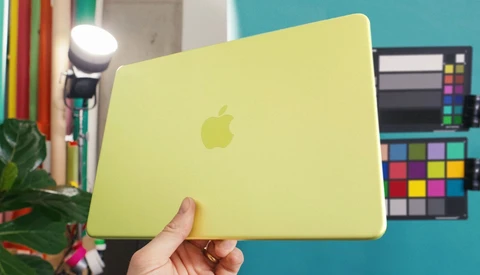 Yellow MacBook held open in a studio with color reference charts visible in the background.