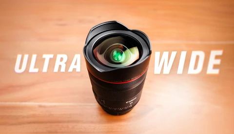 Ultra-wide camera lens with green lens element displayed against warm orange wooden background.