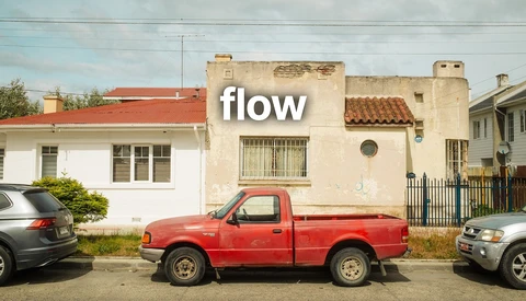 Red pickup truck parked between two cars on a residential street with aging buildings.