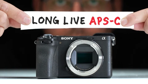 Sony Alpha mirrorless camera body with text banner reading "LONG LIVE APS-C" held above it.