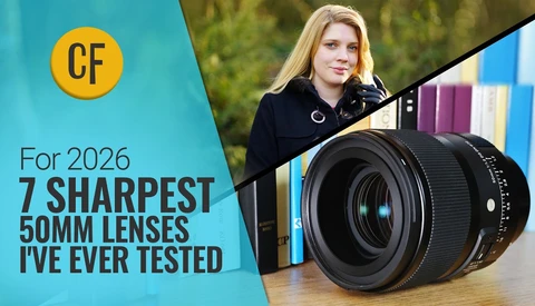 Woman holding a 50mm camera lens with colorful books blurred in the background.