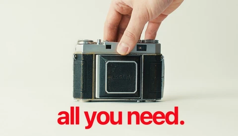 Hand holding a vintage folding camera with squared-off design against a neutral background.
