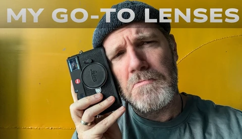 Photographer holding a compact rangefinder camera against a yellow background.