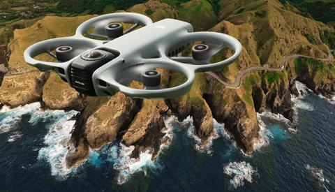 Quadcopter drone hovering above rocky coastal cliffs with crashing waves below.