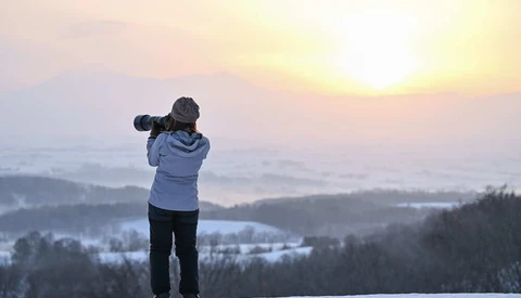 Photographer shooting landscape from snowy hilltop at sunrise