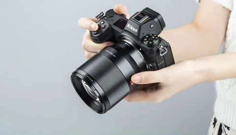 Hands holding a mirrorless camera with attached telephoto lens against gray background