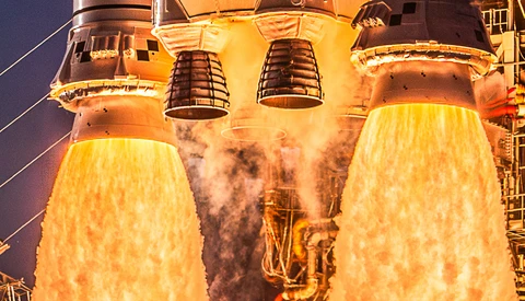 Space shuttle main engines igniting at night, producing bright yellow exhaust plumes against dark sky.