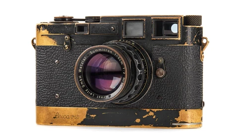 Weathered vintage rangefinder camera with worn brass trim and purple-tinted glass lens element.