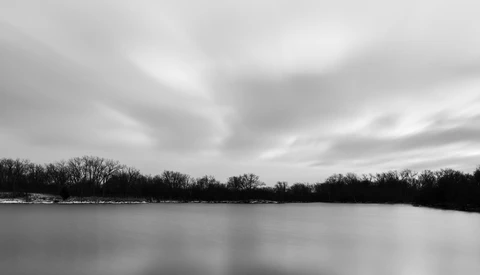 Frozen lake with bare trees along distant shoreline under overcast sky