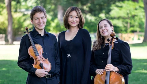 Three musicians in black clothing posing outdoors with violin and cello