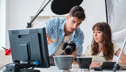 Two photographers review images on a monitor during a studio photoshoot with professional lighting setup.