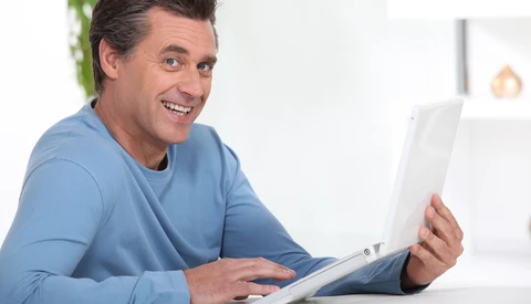 Man in blue long-sleeve shirt smiling while holding and looking at a tablet device.