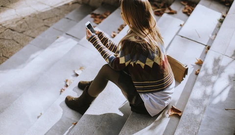 Child sitting on white papers outdoors, holding a striped object, viewed from above with natural shadows.