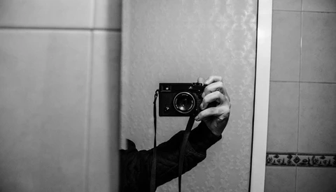 Photographer's hand holding a rangefinder camera in a mirror self-portrait