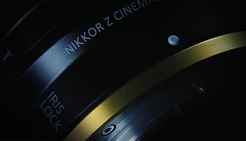Close-up of a Nikkor Z Cinema lens with focus ring and depth of field markings visible against dark background.