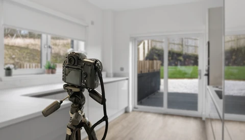 DSLR camera mounted on tripod inside bright, modern kitchen with glass doors overlooking garden.