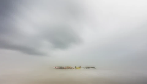 Minimalist landscape with industrial structure barely visible through dense fog and mist