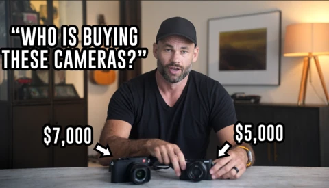 Man in black cap comparing two compact cameras on a table, with price labels of $7,000 and $5,000 visible.