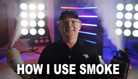Man in glasses and black cap demonstrating lighting technique in front of professional LED panel array.