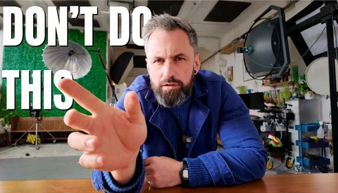 Videographer in blue jacket gesturing toward camera in studio setting with warning text overlay.