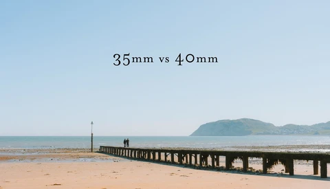 Wooden pier extending into a beach with mountains visible across the water, labeled comparing 35mm vs 40mm focal lengths.
