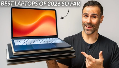 Man gesturing toward a stack of laptops with orange gradient display wallpaper visible on top model.