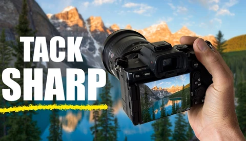 Hand holding a mirrorless camera displaying a sharp landscape photo of a mountain lake on its rear screen.
