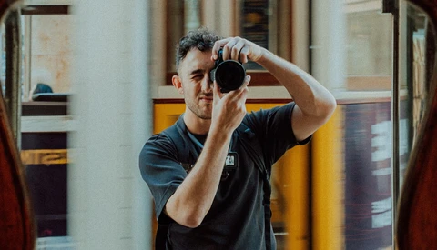 Male photographer looking through camera viewfinder in indoor space.