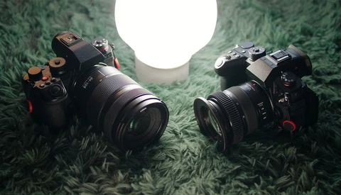 Two professional mirrorless cameras positioned on green textured fabric with a bright circular light source above.