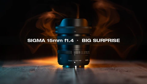 Sigma 15mm f1.4 lens with blue and black coloring positioned on reflective surface with warm atmospheric lighting and smoke effect in background.