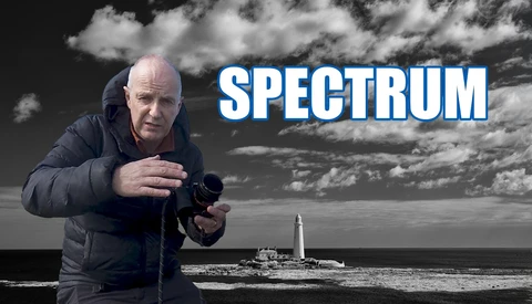 Man in dark jacket holding camera at coastal lighthouse location with dramatic sky.