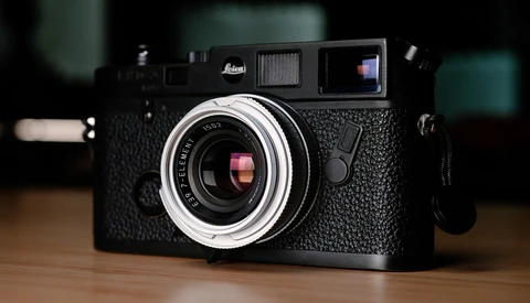 Black Leica rangefinder camera with chrome lens and textured body on wooden surface.